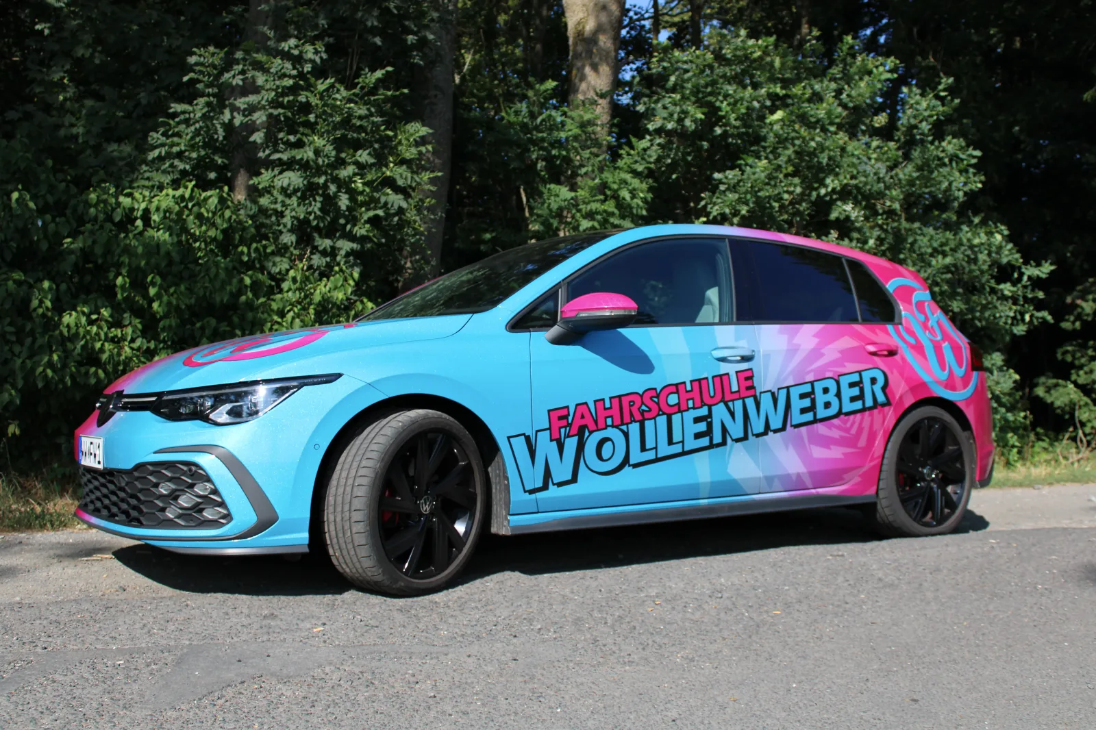 Blau-pink folierter VW Golf der Fahrschule Wollenweber in Seitenansicht.